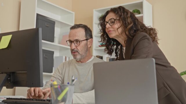 Man smiling and raising hand for high five at computer in office building while colleague leans over and laughs; teamwork celebration joy.