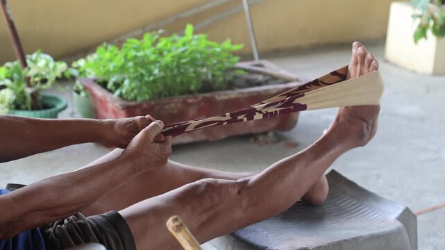 Close up of an old Indian man performing leg stretching exercise using resistance band at home. Senior physiotherapy, knee pain recovery, rehabilitation and healthy aging concept in India.