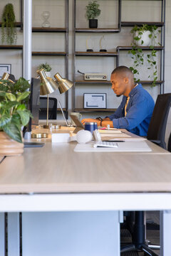 African American man working on laptop at modern office desk wearing blue shirt, copy space