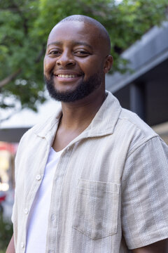 Adult African man standing on city sidewalk wearing light beige shirt, white T-shirt, trimmed beard