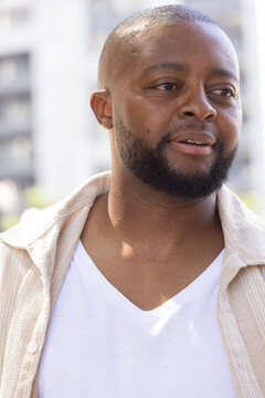 African man gazing slightly right, showing trimmed beard and wearing white V-neck shirt outdoors