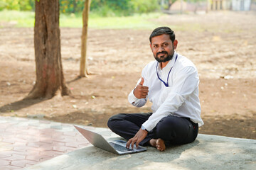 Obraz premium Indian professional sitting outdoors and working on a laptop, representing modern digital work and rural connectivity.