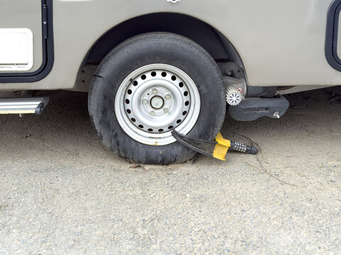 View of a flat tire on a motorhome wheel with a yellow security wheel lock attached while parked on a gravel ground Sariyer, Istanbul, Turkiye.