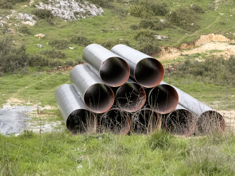 View of large industrial metal pipes with red interiors stacked in a pyramid on a grassy field with green hills Sariyer, Istanbul, Turkiye.