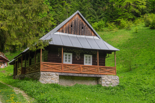 View of a traditional wooden house at the Former charcoal workers settlement Moce with a stone foundation and porch on a green hillside in Motycky, Banska Bystrica Regio, Slovakia.