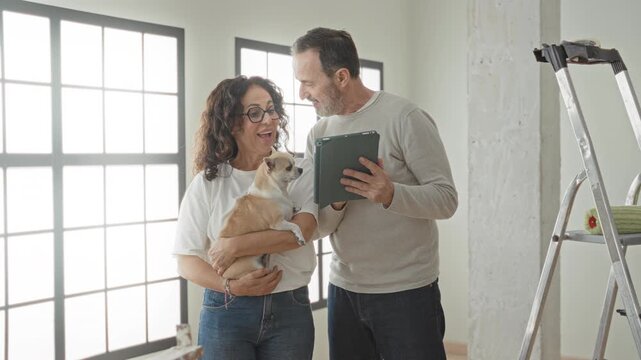 Middle aged couple with dog, woman pointing and man holding tablet in building; home renovation planning calm.