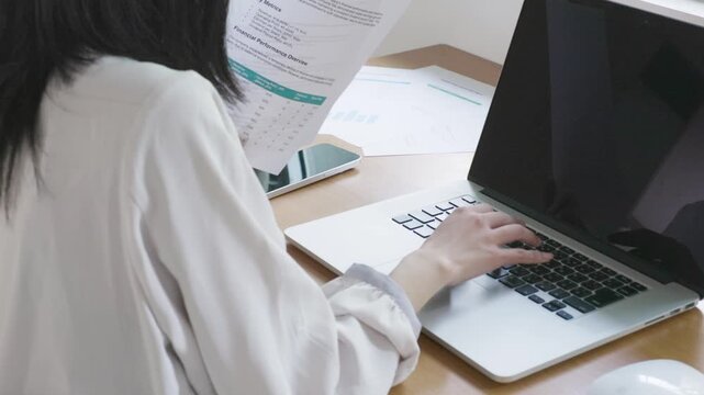 Close-up of woman's hands holding business document while working on laptop