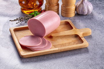 Boiled pink sausage log with slices on wooden board © Andrei Starostin