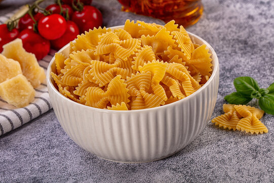 Dry farfalle pasta in white bowl with fresh ingredients