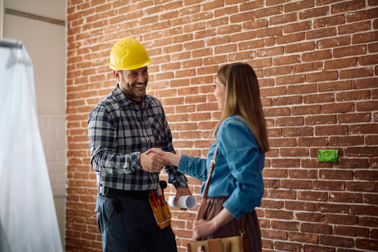 Happy building contractor greeting female customer on site.