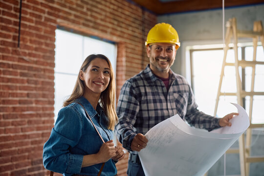 Happy woman and construction worker analyzing blueprints during home remodeling project.
