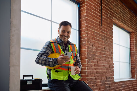 Happy construction worker using mobile phone on coffee break.