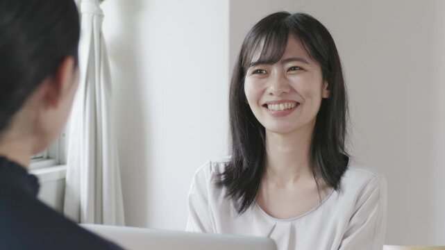 Young Asian woman smiling and talking while using laptop