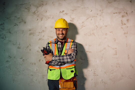 Happy building contractor standing with arms crossed against wall and looking at camera.