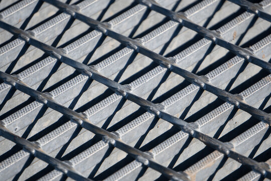 Close Up Of Metal Drain Grating On A Road Surface（道路にあるグレーチングの金網のクローズアップ）