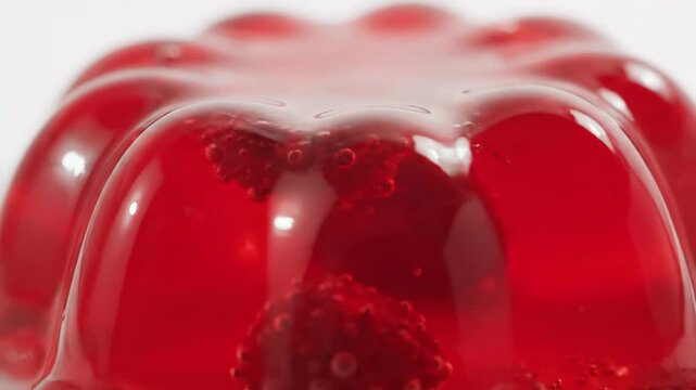 Vibrant red gelatin dessert in a fluted mold with embedded berries, featuring a delicious and wobbly macro close-up on a bright background