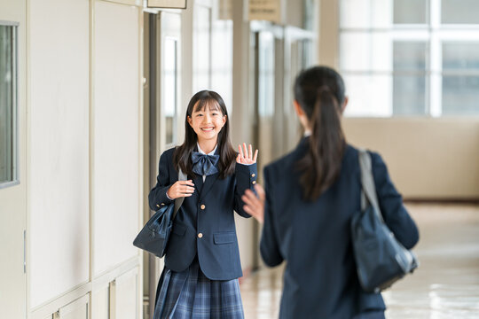 Elementary, middle, and high school girls in uniform walking down a school corridor.