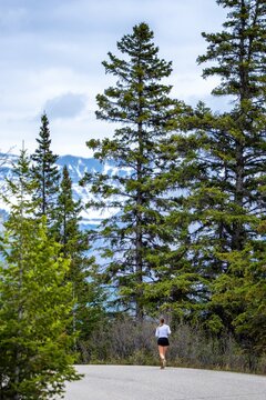 Woman running on mountain road with green trees and snowy peaks