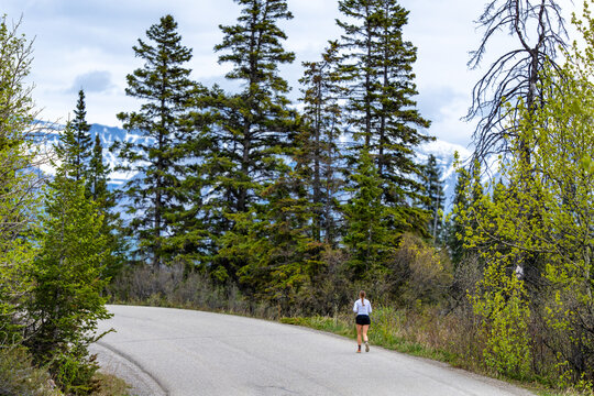 Woman running on mountain road with green trees and snowy peaks