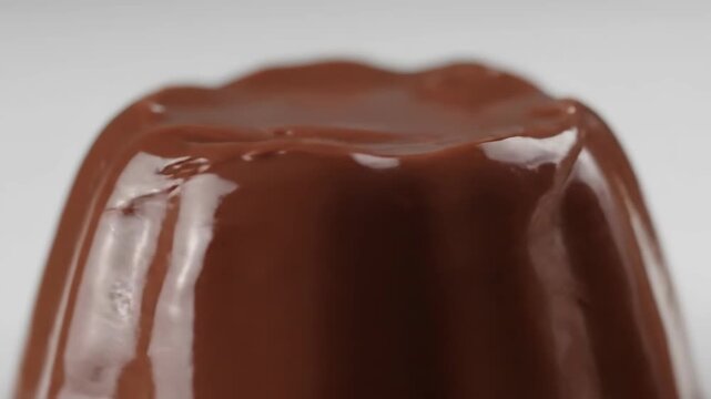 Macro shot of rich and glossy chocolate pudding, custard, or caramel flan dessert isolated on a white background, highlighting the smooth texture and deep brown color.