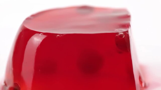 Macro close-up of vibrant red gelatin dessert on a white background showing translucent texture, air bubbles, and glossy surface