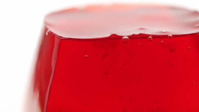 Extreme close-up of vibrant red gelatin dessert surface with air bubbles isolated on a white background, showcasing the glossy, translucent texture.