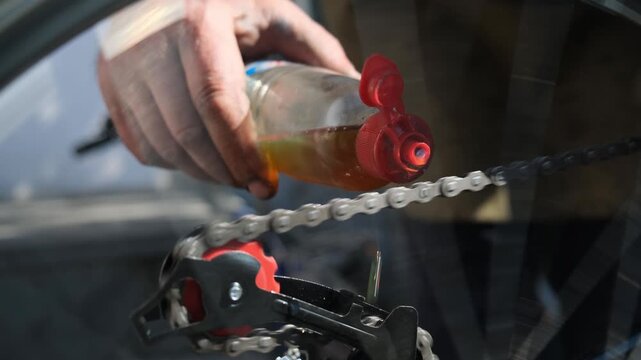 Transmission oil applied in thin stream onto chain for lubrication and wear reduction. Bicycle mechanic lubricating drivetrain. Service and maintenance of cycling transport. Repair of bicycles