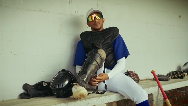 Young baseball catcher sits in the dugout, meticulously adjusting his protective gear. He is focused and ready for the intense competition ahead.