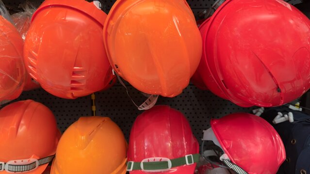 Orange and red construction hard hats on retail display rack industrial safety helmets background