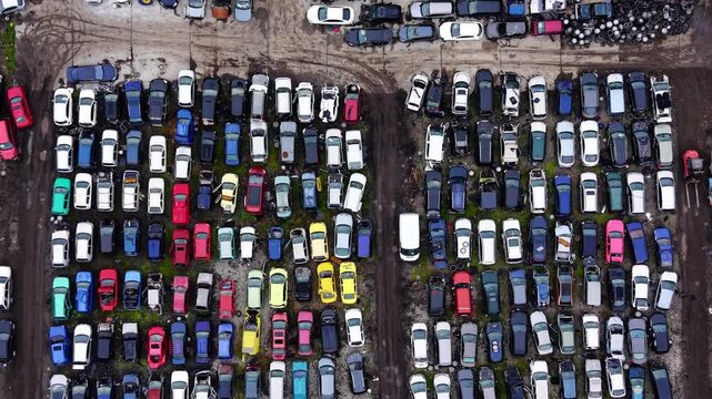 Overhead view of scrapyard with tire pile and vehicle rows, Bulgaria. Multicolored junked cars, stacked tires and dirt access lanes on overcast day. Aerial view.