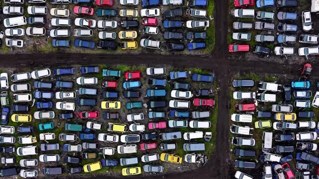 Aerial top-down pattern of salvage cars in four sections, Bulgaria. Drone view of colorful wrecked vehicles divided by dark dirt pathways forming cross shaped grid.