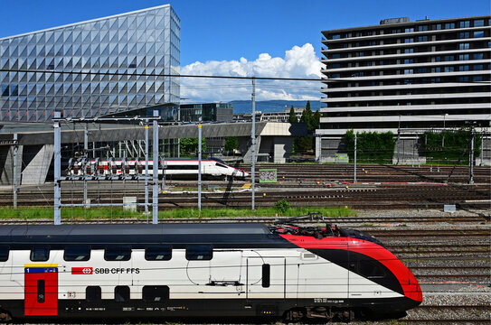 Geneva, Switzerland, Europe - 05.2026 : Stadler KISS and fast Stadler SMILE Swiss - Electric multiple unit trains, JTI headquarters of Japan Tobacco International, Picciotto students house at right