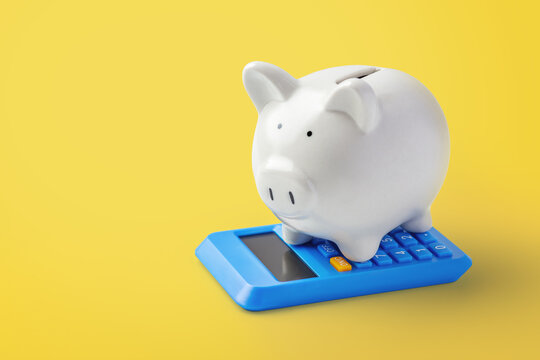 White piggy bank on a blue calculator over yellow background. Financial planning, savings, and investment concept