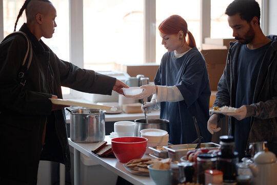 Young adult volunteers serving meals to people in need at humanitarian aid center, supporting community relief and food assistance. Ideal for charity campaign, social support messaging
