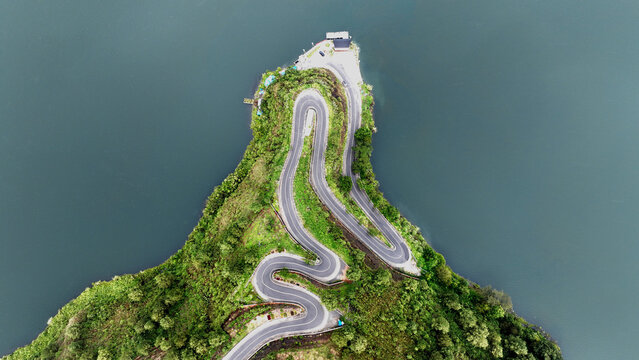 Aerial view of the winding Sibea Bea road on a lush green peninsula surrounded by the calm waters of Lake Toba in Samosir Regency, North Sumatra, Indonesia.