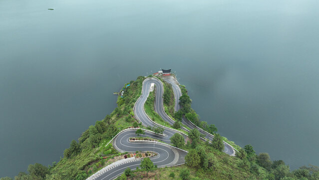 Aerial view of Sibea Bea hill featuring a winding serpentine road and traditional Batak architecture overlooking Lake Toba in Samosir Regency, North Sumatra, Indonesia.