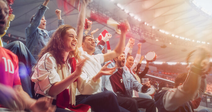 Portrait of Woman in a White Jacket and Red Scarf Smiles and Claps as Soccer Football Championship Supporters Around Her Rise From Stadium Seats, Raise Arms, and Celebrate a Goal Together.