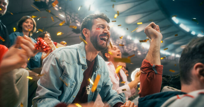 Portrait of White Male Soccer Football Supporter With Diverse Male and Female Fans, Hands Raised, Smiling and Excited as Gold Confetti Fills Packed Championship Stadium During Cup League Match