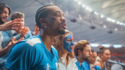 Side Profile Portrait of Black Male Soccer Football Supporter, Clapping Among Packed Stadium Fans, Happy Cheer and Excited Focus During Championship Cup League Match in Crowded Arena Stands. © Gorodenkoff