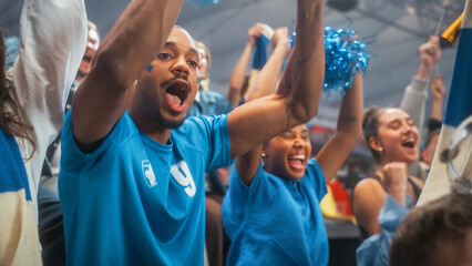 Fototapeta premium Close Portrait of Black Male Soccer Football Supporter With Blue Face Paint, Arms Raised in Excited Cheer as Diverse Stadium Crowd Waves Scarves During Championship World League Cup Match Celebration
