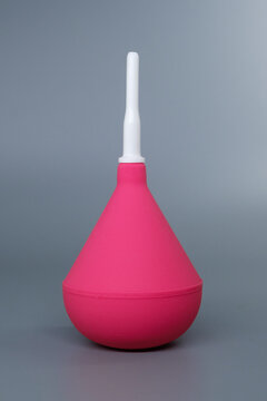 Pink medical syringe bulb with a white plastic tip on a grey background. Disposable rubber enema bulb pump with removable plastic nozzle.
