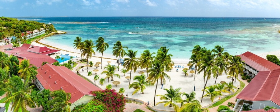 Aerial view of Long Bay featuring a luxury resort with red rooftops, white sandy beach, palm trees overlooking turquoise waters in Saint John's, Saint John, Antigua and Barbuda.