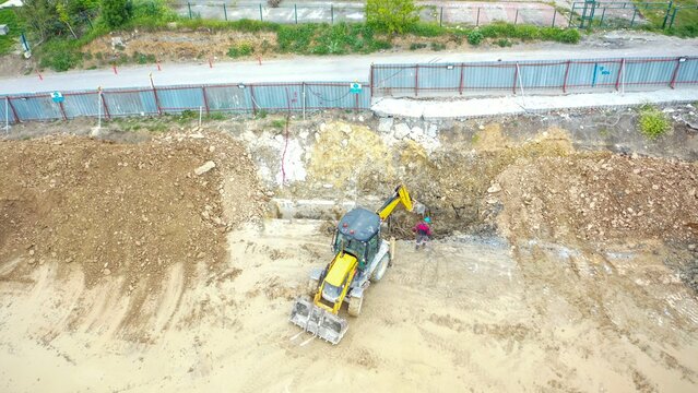 Aerial view of a yellow excavator working on a construction site with a worker standing on the dirt ground in Avcilar, Istanbul, Turkiye.