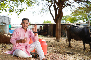 Fototapeta premium Happy indian farmer using smartphone at dairy farm