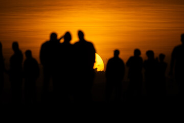 Fototapeta premium Group of people standing together during sunset at a scenic location with bright orange sky in the background