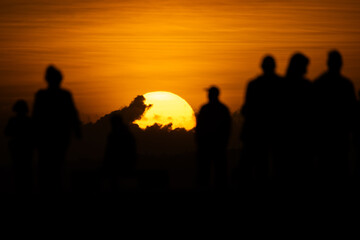 Fototapeta premium People watch sunset at the beach while the sky shows orange and yellow colors in the background during the evening