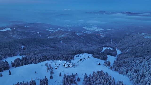 Aerial backward flight during blue hour revealing Hala Miziowa mountain shelter in winter mist