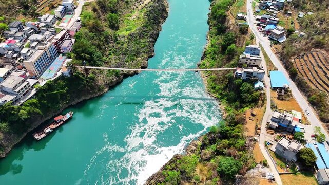 Aerial of Pedestrian Cable Bridge Over Winding River in Karst Mountains, Isolated Hamlet on Bank