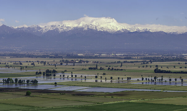 Aerial view of flooded rice fields and rural landscape with snow-capped mountains in the background San Germano Vercellese, Piedmont, Italy.