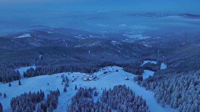 Drone orbit shot of Hala Miziowa mountain shelter during winter blue hour with misty mountains